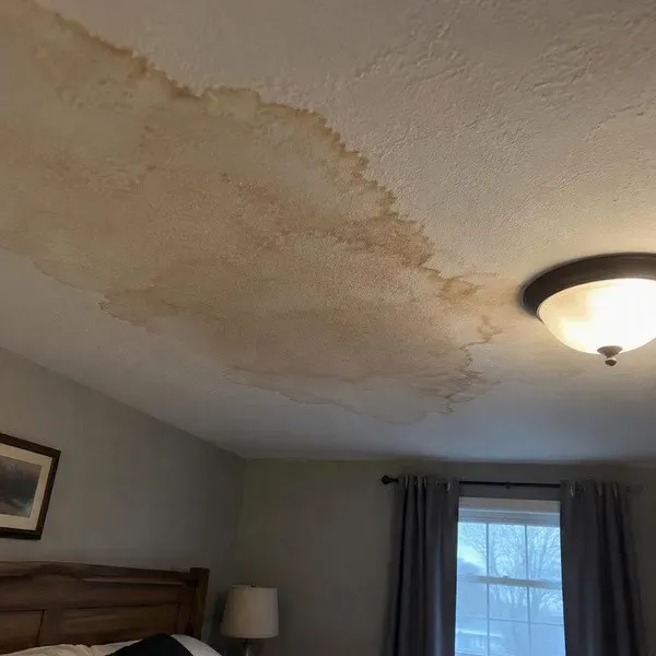 Brown water stain spreading across a bedroom ceiling from a roof leak