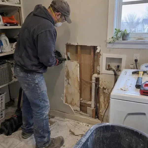 Cutting out water-damaged drywall in a laundry room after a pipe leak