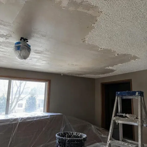 Popcorn ceiling partially scraped away to show smooth drywall sections underneath