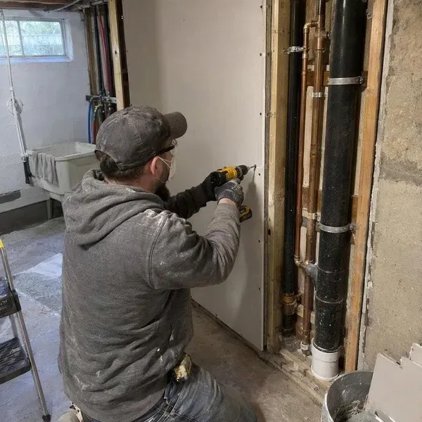 Replacement drywall fastened beside utility pipes after a leak